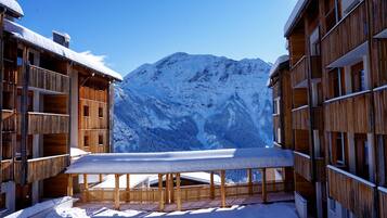 Un edificio de madera con balcones y una mesa cubierta de nieve en primer plano, con una montaña al fondo.