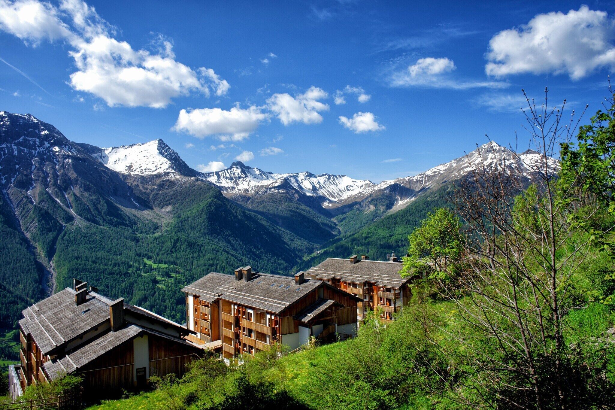 Un pueblo de montaña con casas de madera, un valle y picos nevados.