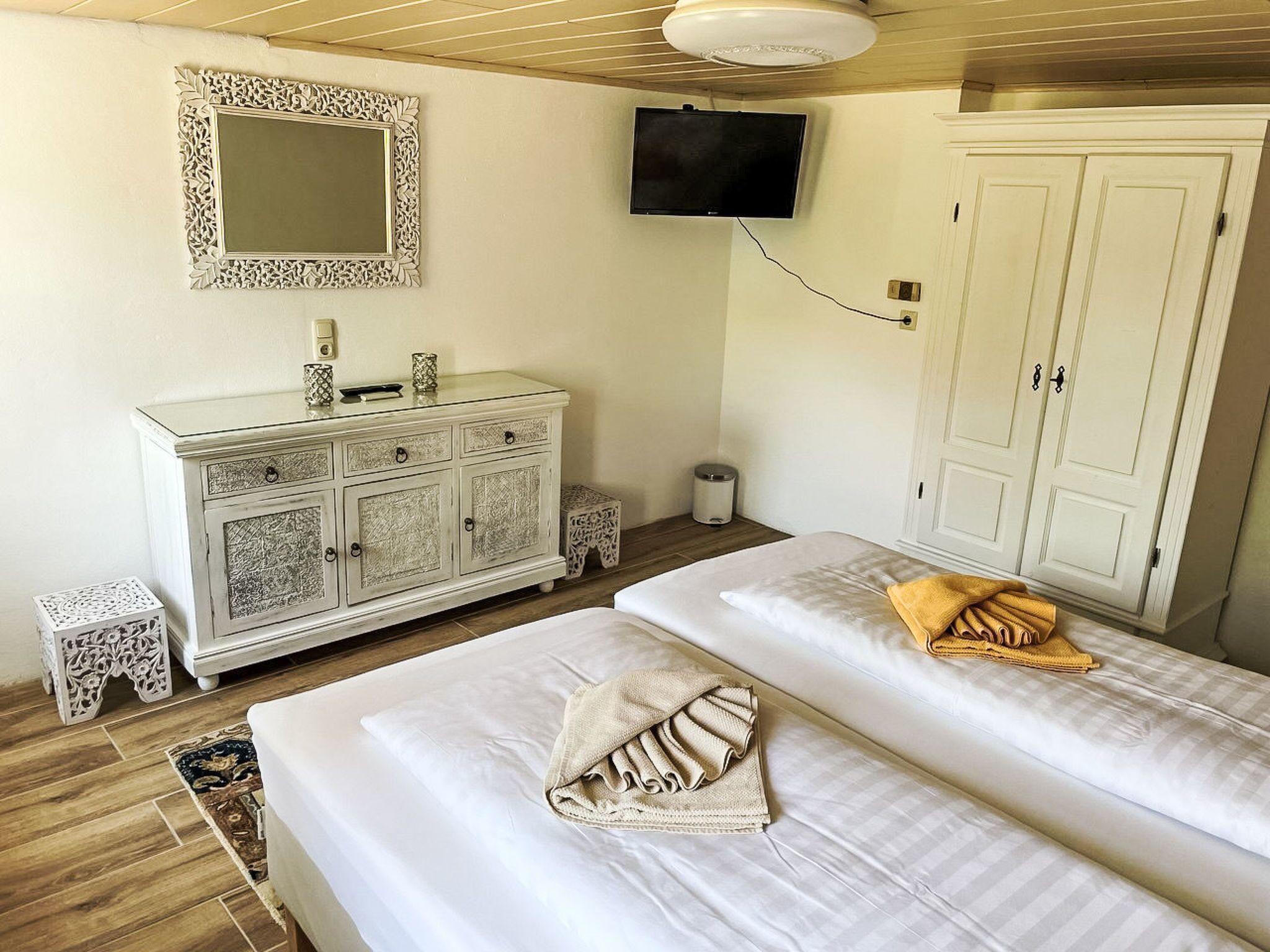 Ein Zimmer mit zwei Betten, einer weißen Kommode, einem an der Wand montierten Fernseher und einer weißen Tür.