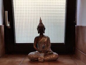 Une statue de Bouddha en position méditative, assise en posture du lotus, avec une fenêtre à motifs derrière.