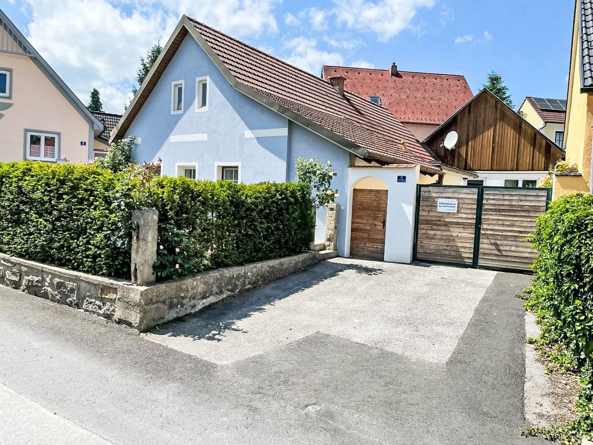 A residential building with a sloped roof, a gated entrance, and a well-maintained hedge.