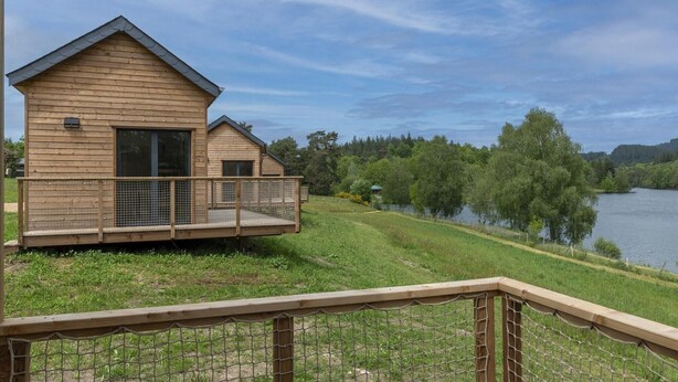 A wooden cabin with a balcony overlooking a lake, surrounded by greenery. - Cabin near Meyrignac Lake (MEYRIGNAC  L'EGLISE)