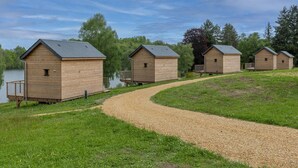 A row of wooden cabins with a gravel path leading to a body of water. - Cabin near Meyrignac Lake (MEYRIGNAC  L'EGLISE)