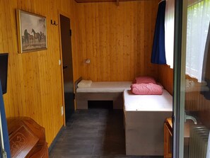 Une petite pièce aux murs en bois, un lit avec un matelas et des oreillers, une petite table et un tableau accroché au mur.