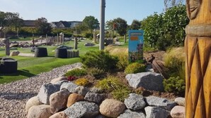 Un parque con una escultura de madera, un cartel y una zona verde con rocas.