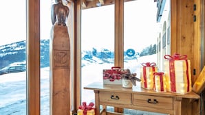 En interiör med träinredning, ett fönster med utsikt över snötäckta berg, en träskulptur och ett bord med inslagna presenter.