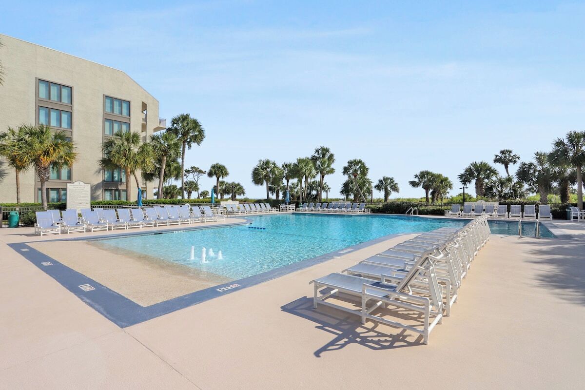 A pool area with lounge chairs and palm trees.