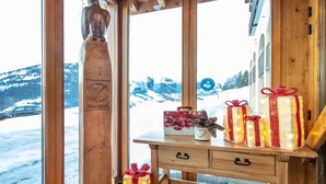 Ein Holzinnenraum mit Blick auf verschneite Berge, eine Holzskulptur und ein Tisch mit verpackten Geschenken.