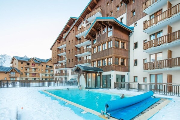 Un hôtel à plusieurs étages doté de balcons en bois, d’une piscine et, au loin, d’une piste de ski.