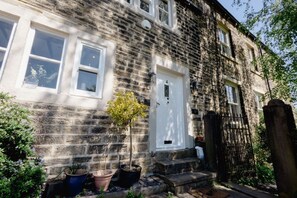 A stone building with a white door, windows, and steps leading to the entrance. - Robin Cottage | Stylish Countryside Escape (Honley)