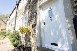 A stone building with a white door, potted plants, and a small window. - Robin Cottage | Stylish Countryside Escape (Honley)