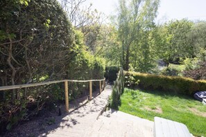 A paved pathway leading through a garden with various shrubs and trees. - Robin Cottage | Stylish Countryside Escape (Honley)