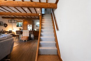 A staircase with wooden beams and carpeted steps leading to a kitchen area with wooden cabinets and a dining area with a sofa and chairs. - Robin Cottage | Stylish Countryside Escape (Honley)