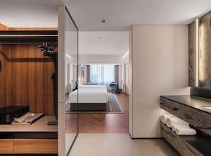 Ett modernt hotellrum med en garderob i trä, en stor säng, ett badrum med spegel och utsikt över staden.