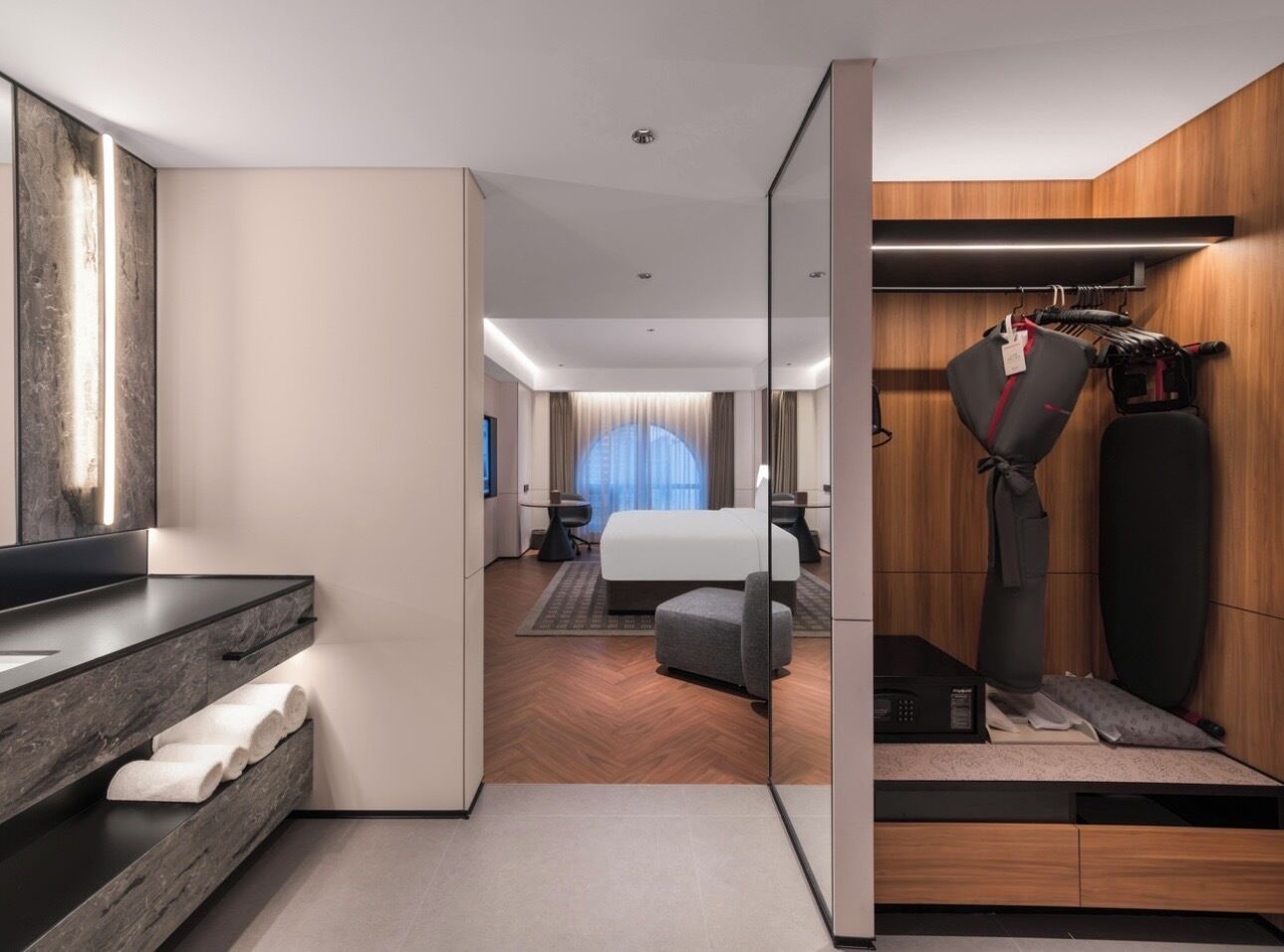 Une chambre d’hôtel moderne dotée d’un grand lit, d’un coin salon, d’une coiffeuse avec miroir et d’un espace dédié à l’exercice physique.