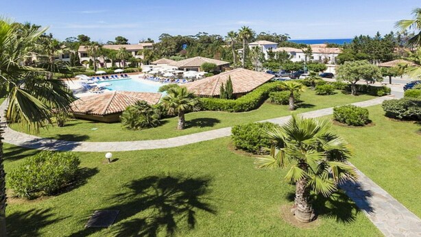 Um resort com piscina, palmeiras e vista clara do oceano.