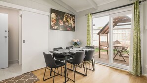 Uma sala de jantar com mesa e cadeiras, um quadro na parede e vista para o exterior.