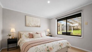 Quarto com uma cama grande, duas mesas de cabeceira, uma janela com vista para o quintal e uma luminária no teto.