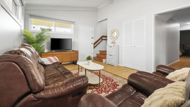 Sala de estar com um sofá de couro marrom, uma televisão, uma mesinha e um tapete com padrão vermelho e branco.