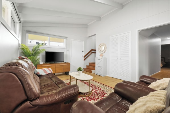 Ein Wohnzimmer mit einem braunen Ledersofa, einem Fernseher, einem kleinen Tisch und einem roten und weißen Teppich.