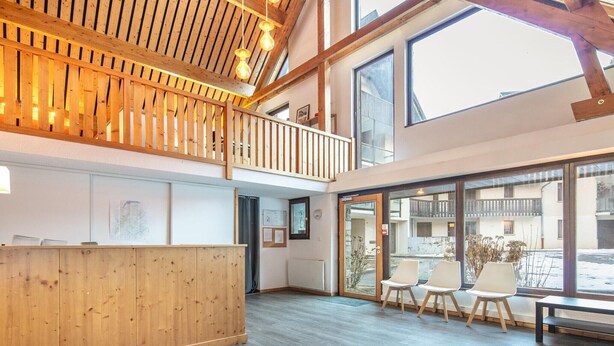 A reception area with a wooden reception desk, a balcony with a railing, and large windows offering a view of the outside. - Mountain Lodging with Private Balcony (Saint  Colomban  des  Villards)