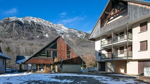 A modern building with a wooden facade, large windows, and a balcony overlooking a snowy landscape with mountains in the background. - Mountain Lodging with Private Balcony (Saint  Colomban  des  Villards)