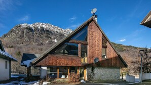 Una casa moderna de dos pisos amb teulada inclinada, grans finestres i fonaments de pedra.