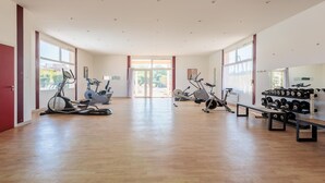 Et rummeligt fitnessrum med træningsudstyr, store vinduer og trægulv.