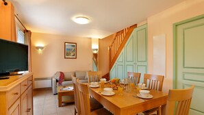 A dining area with a wooden table set for breakfast, a television on a stand, and a staircase leading to an upper level. - 3-Room Holiday Home in the Var (TOURRETTES)