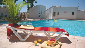 Área da piscina com espreguiçadeiras, mesa com frutas e bebidas, e uma piscina azul cristalina.