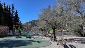 Un parc infantil amb tobogan, cadira de balanceig i zona de jocs verda.