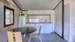 Cuina compacta amb armaris blancs, microones i un rentaplat. Hi ha una taula rodona amb cadires, i una finestra amb vista a vegetació exterior.
