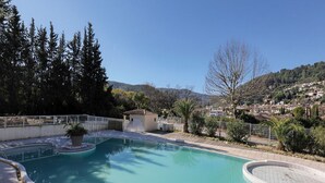Una piscina amb vora corba, envoltada d'una tanca blanca, i vista a un turó amb cases.