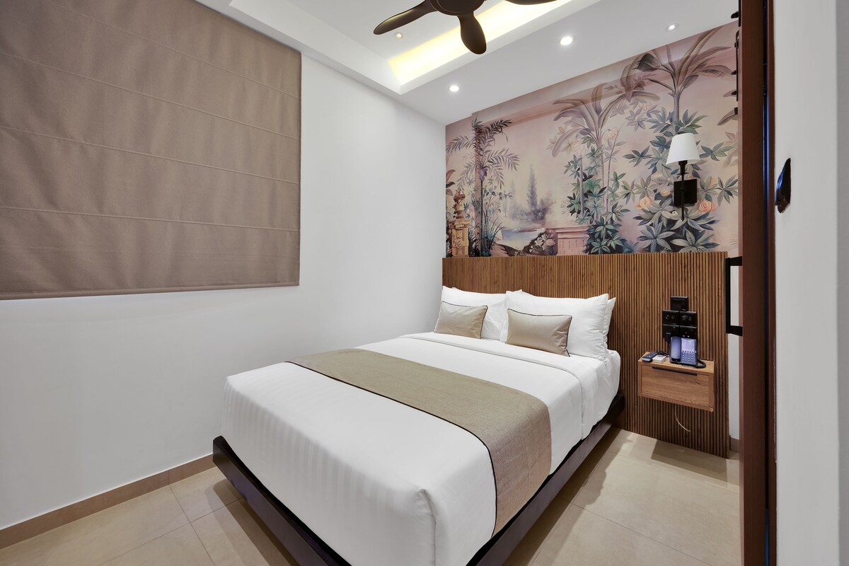 A modern hotel room with a large bed, a nightstand with a lamp, and a decorative mural on the wall.