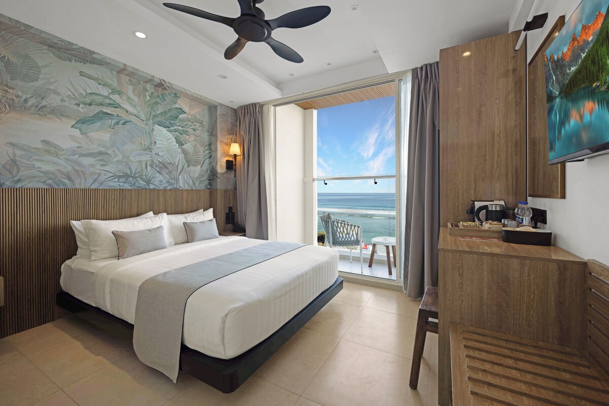 Ein Hotelzimmer mit Bett, Schreibtisch, Stuhl, Deckenventilator, Fernseher und Blick aufs Meer.