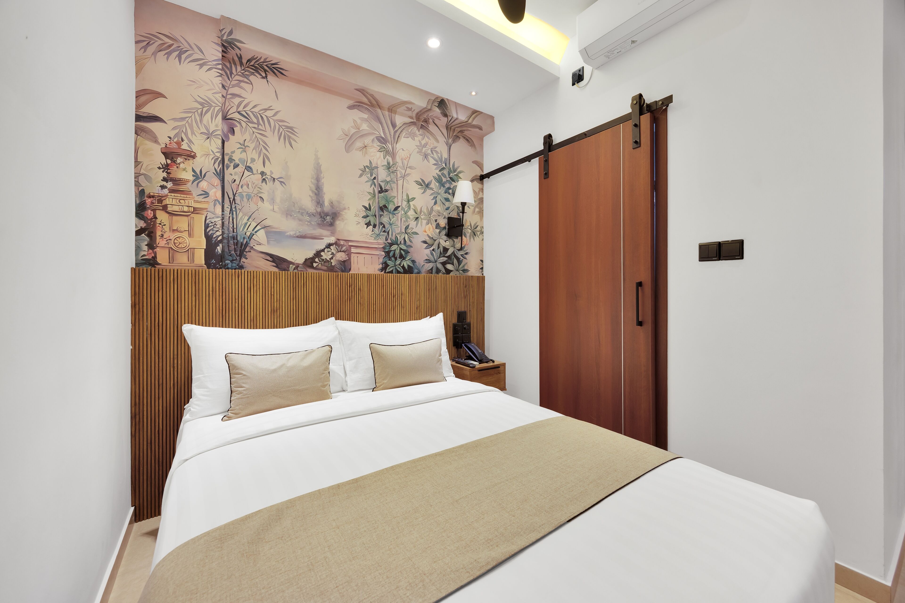 Ein Hotelzimmer mit einem Bett, einem Holz-Kopfteil, einem Wandbild, einer Schiebetür und einem Nachttisch mit einer Lampe.