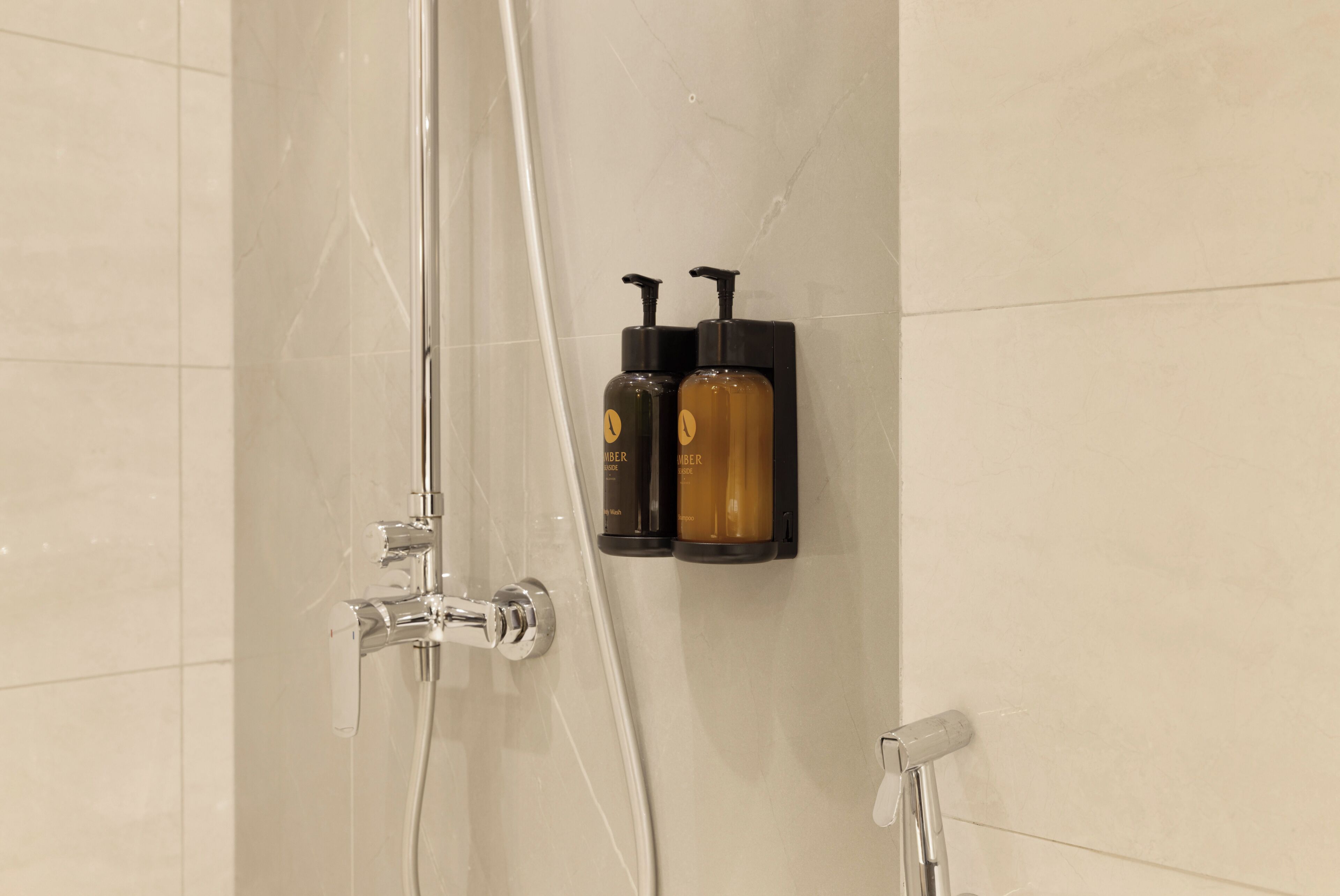 Ducha con puerta de vidrio, cabezal de ducha de mano y dos botellas de champú sobre un jabonera negro.