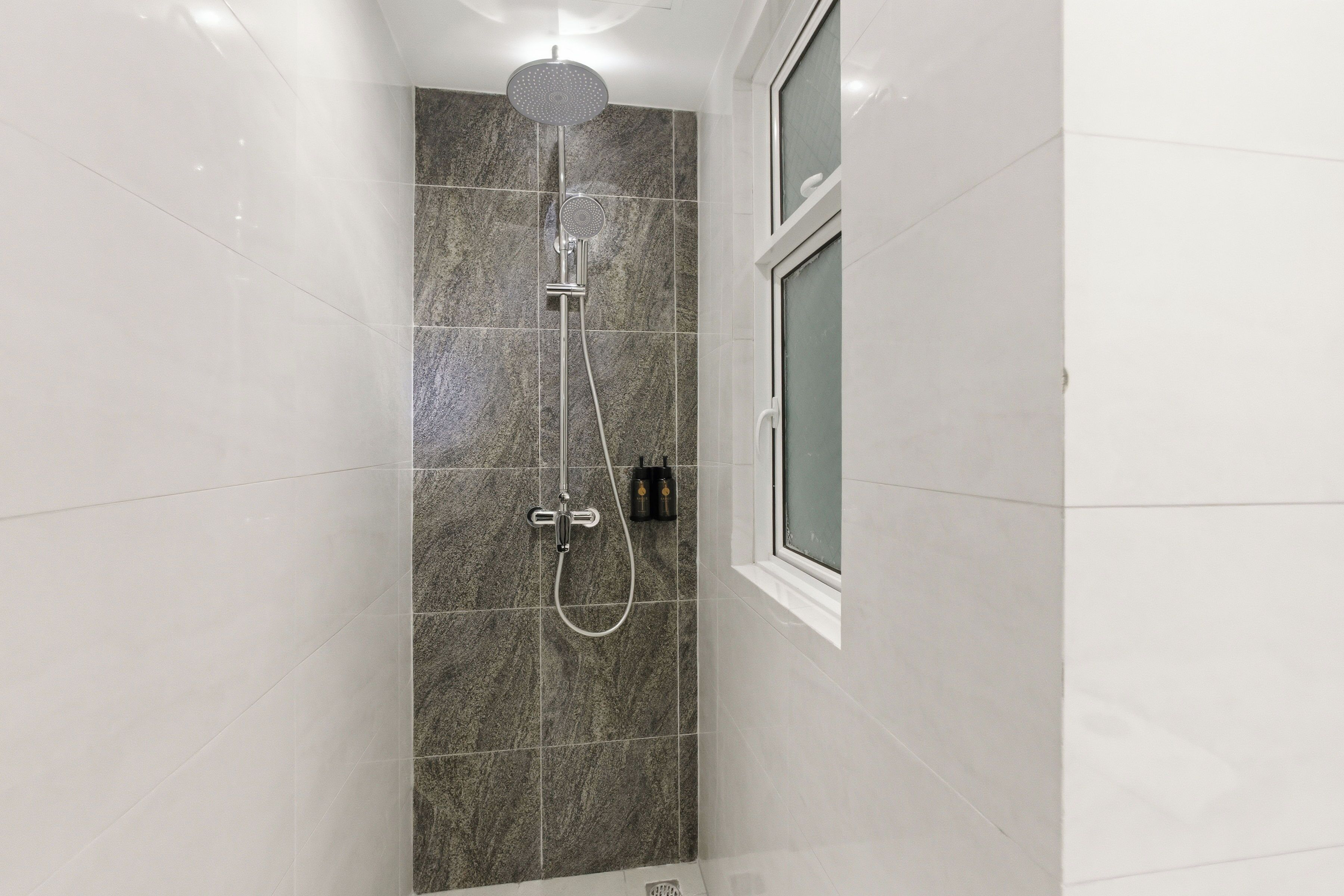 A shower with a handheld showerhead, a wall-mounted faucet, and a control panel.