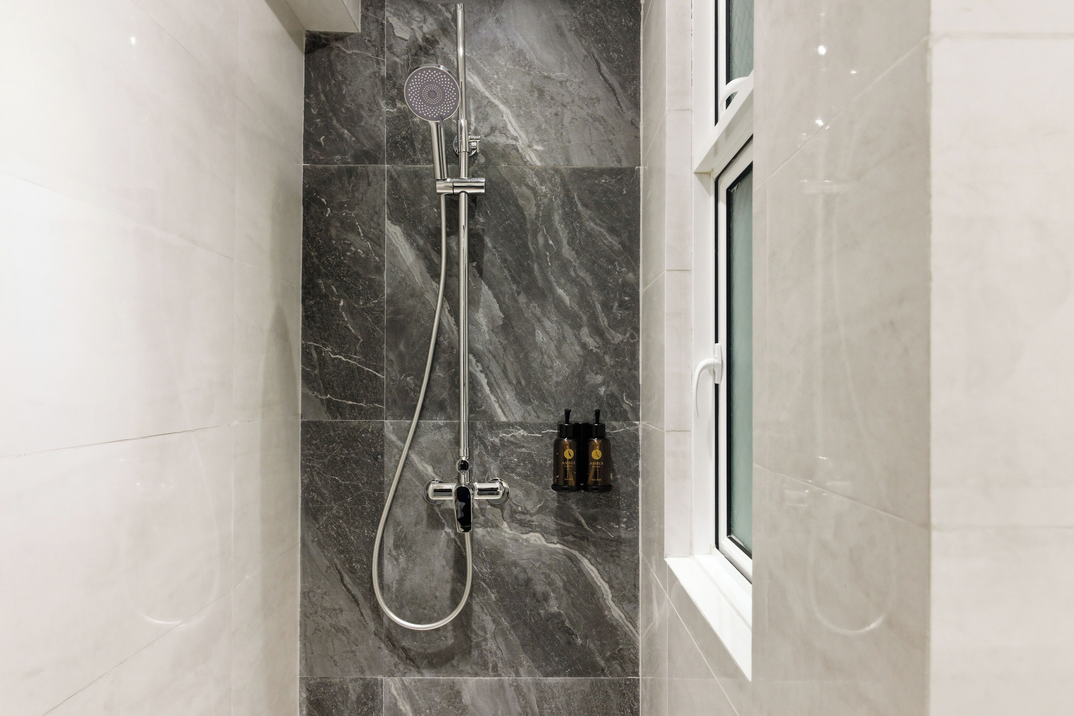Un baño moderno con ducha, azulejos de mármol y ventana.