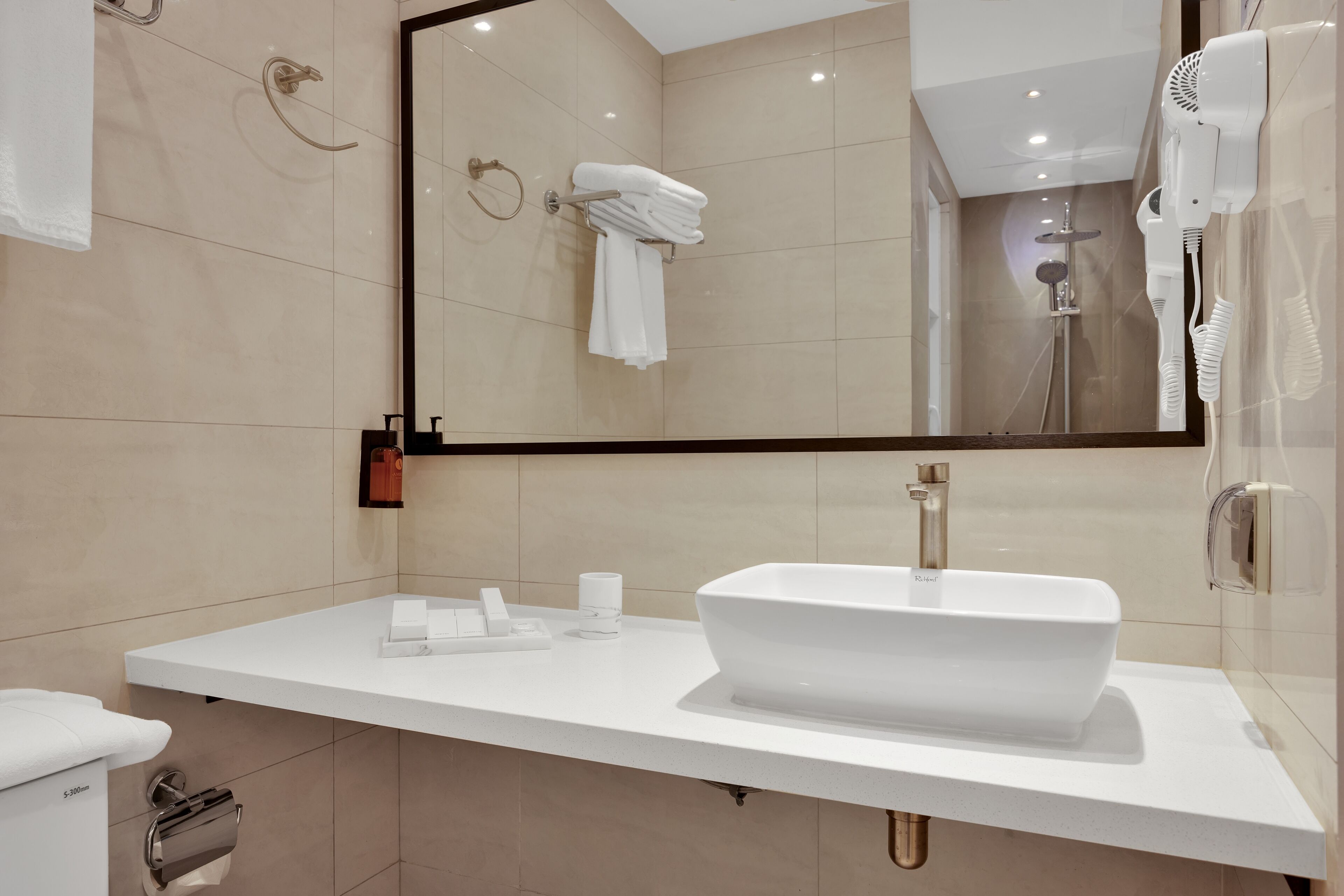 A modern bathroom with a large mirror, white sink, and towel rack.