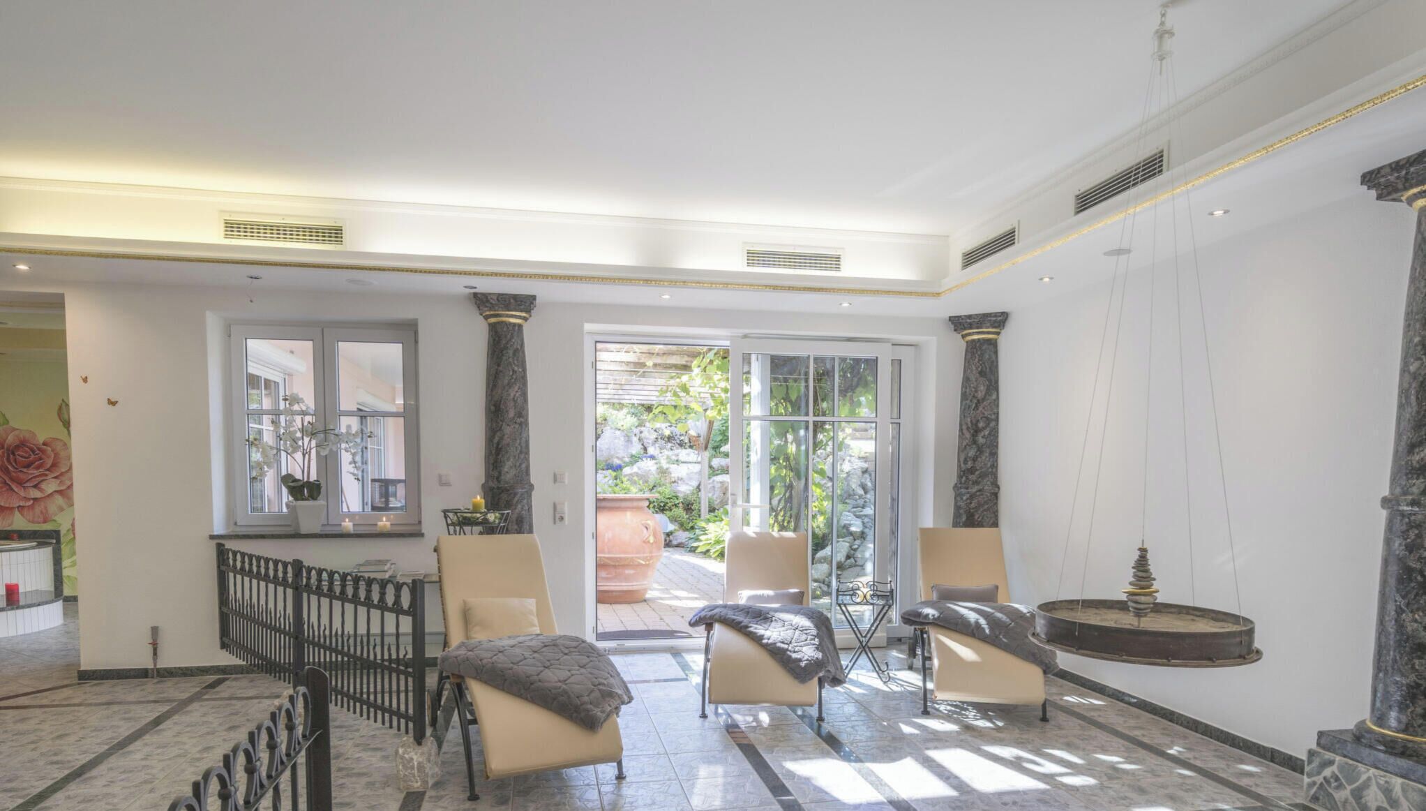 Eine großzügige Lobby mit Marmorboden, zwei Sesseln, einem großen Fenster und Blick auf den Garten.