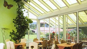 Uma estufa com teto de vidro, móveis de vime e vista para um jardim.