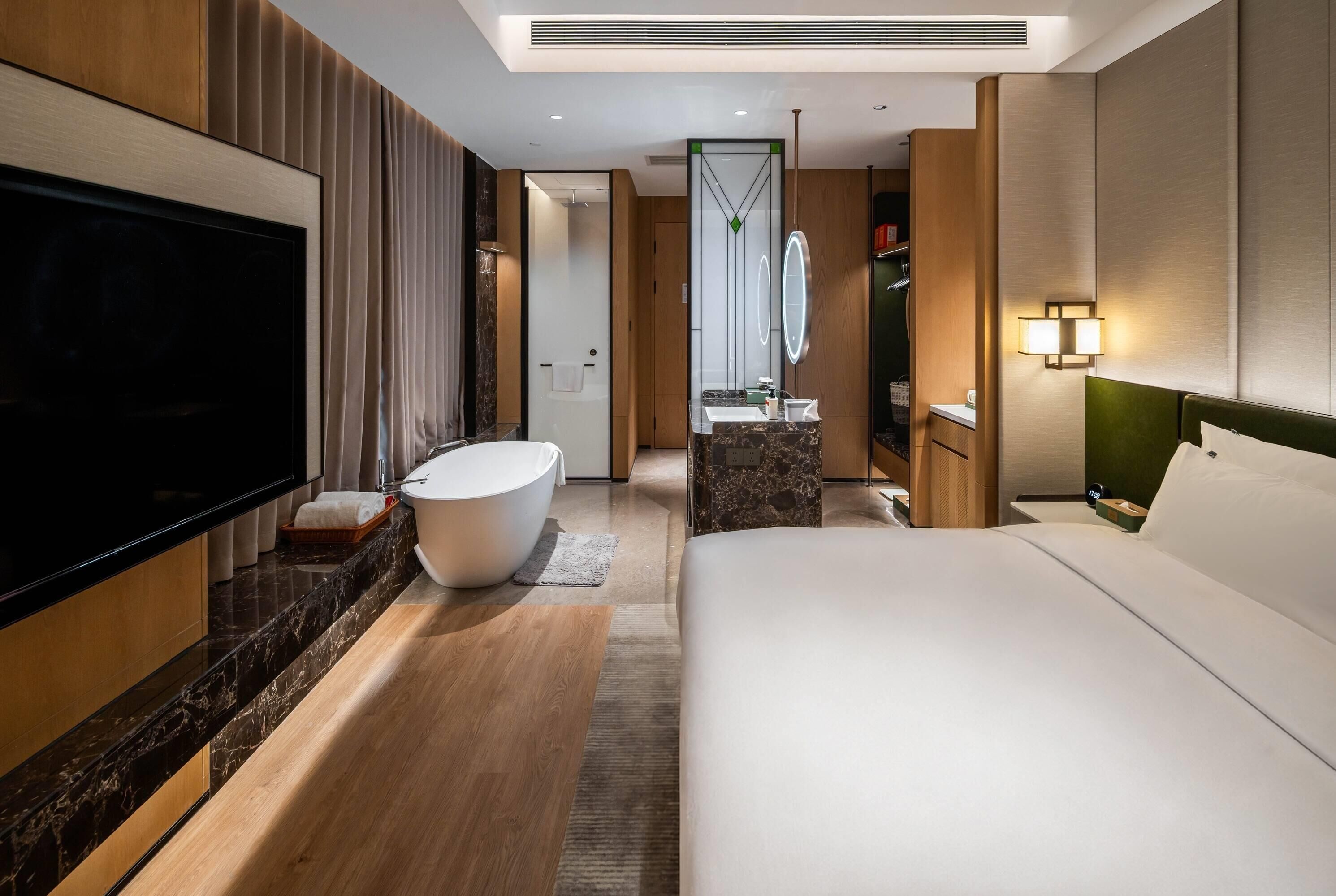 Habitación de hotel moderna con una cama grande, una bañera, un tocador con espejo y un televisor a la izquierda.