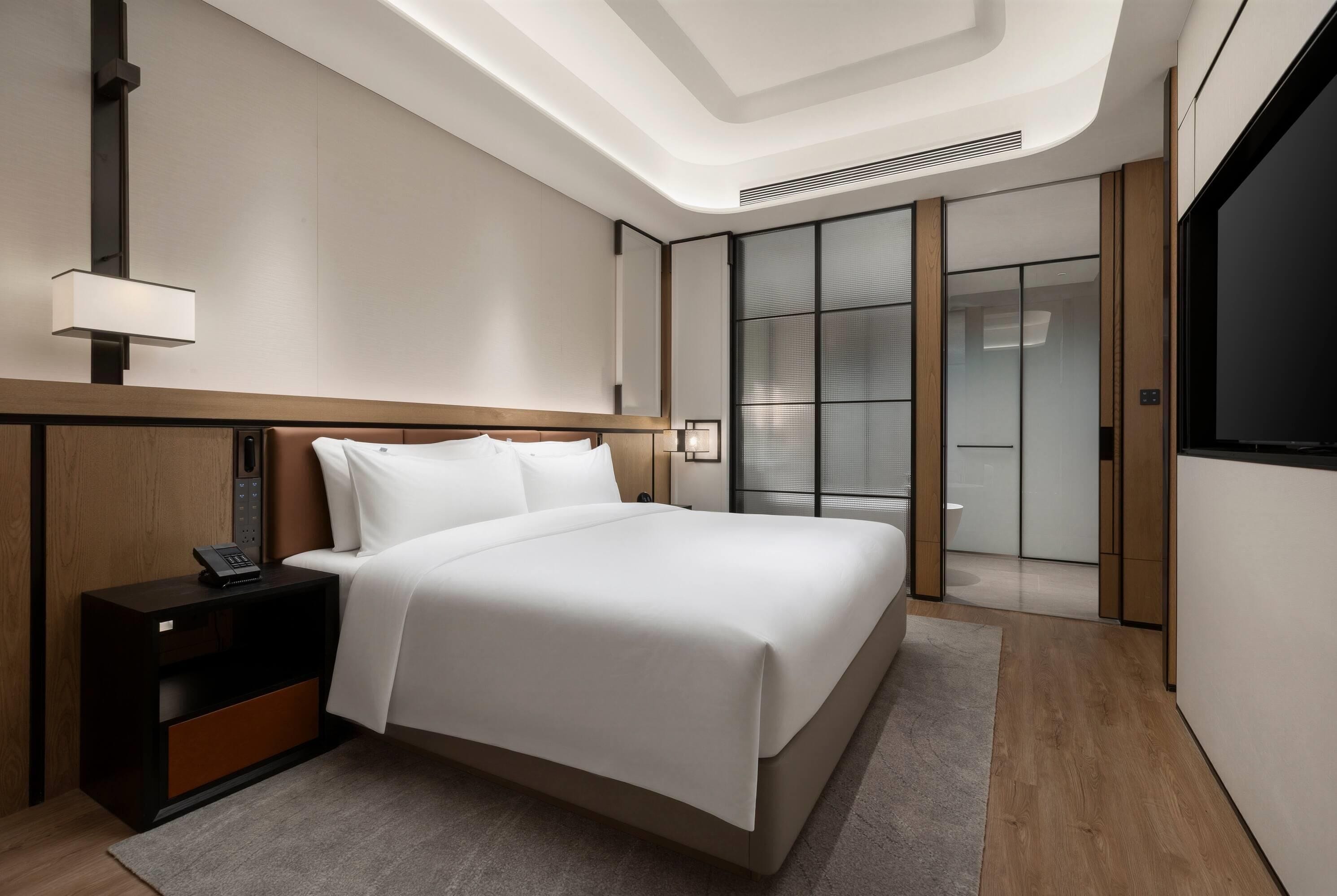 A modern hotel room with a large bed, bedside table, and a nightstand with a phone.
