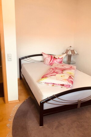 Ein Einzelbett mit floralem Überwurf, einer Nachttischlampe und einem kleinen Tisch.