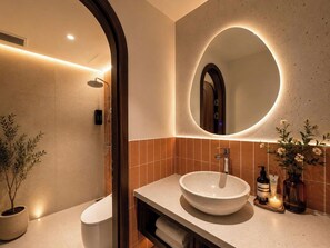 Une salle de bain moderne avec un miroir rond, un lavabo sur colonne, une douche et une plante en pot.