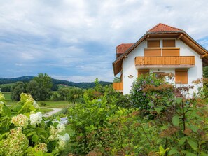 Una casa con balcón, rodeada de abundante vegetación y cielo despejado.