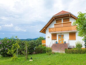 Una casa de dos pisos con un balcón, una puerta principal con un diseño de cruz y un jardín con flores y vegetaci ón.