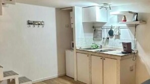 Cocina compacta con suelo de madera, armarios blancos y una pequeña encimera.