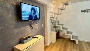 Un interior moderno con un televisor de pantalla plana montado en una pared de pizarra, un mueble blanco y una escalera de madera.
